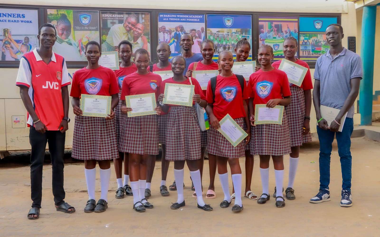 Students holding certificates in front of a school building