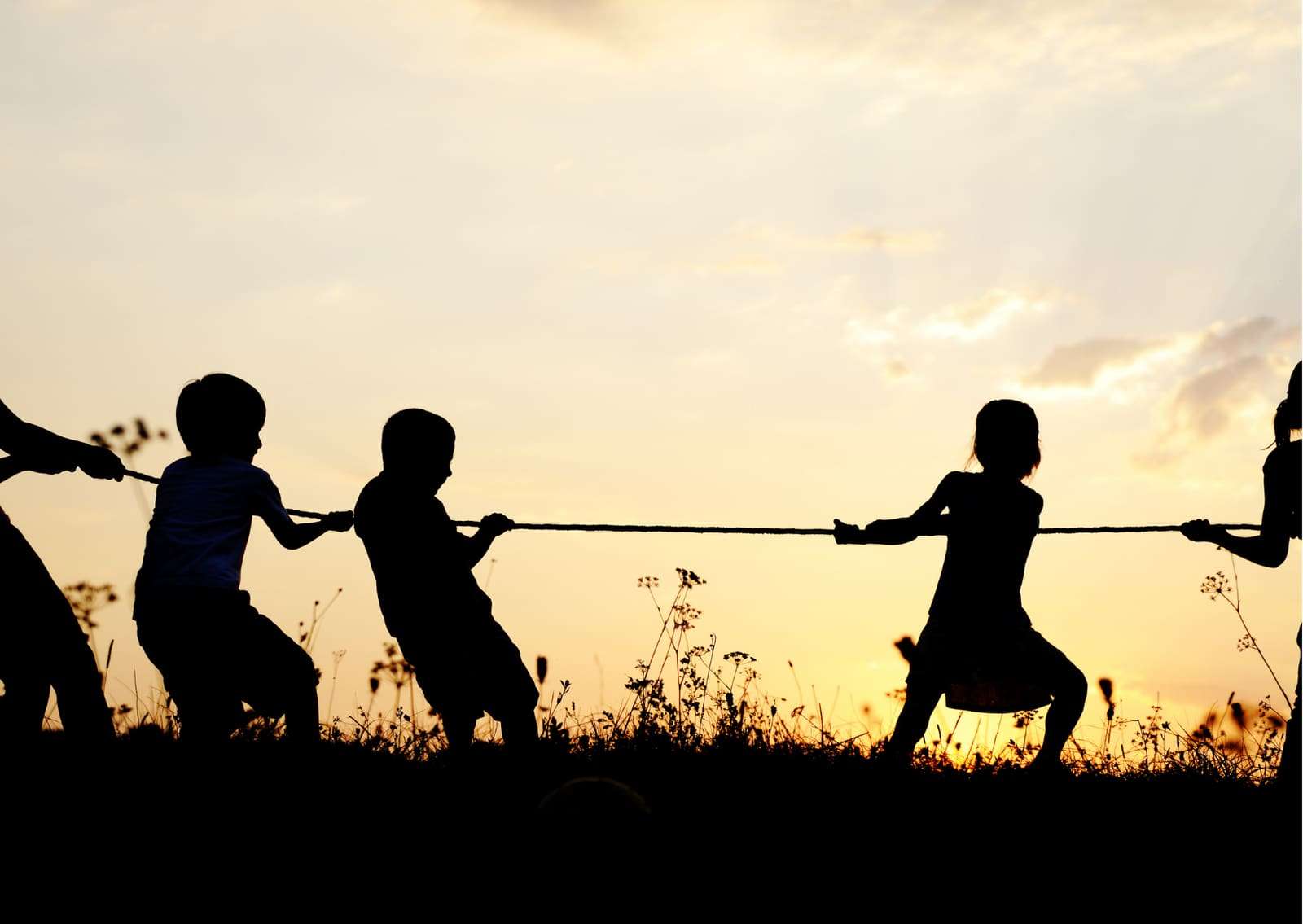 Silhouettes of children playing tug of war at sunset