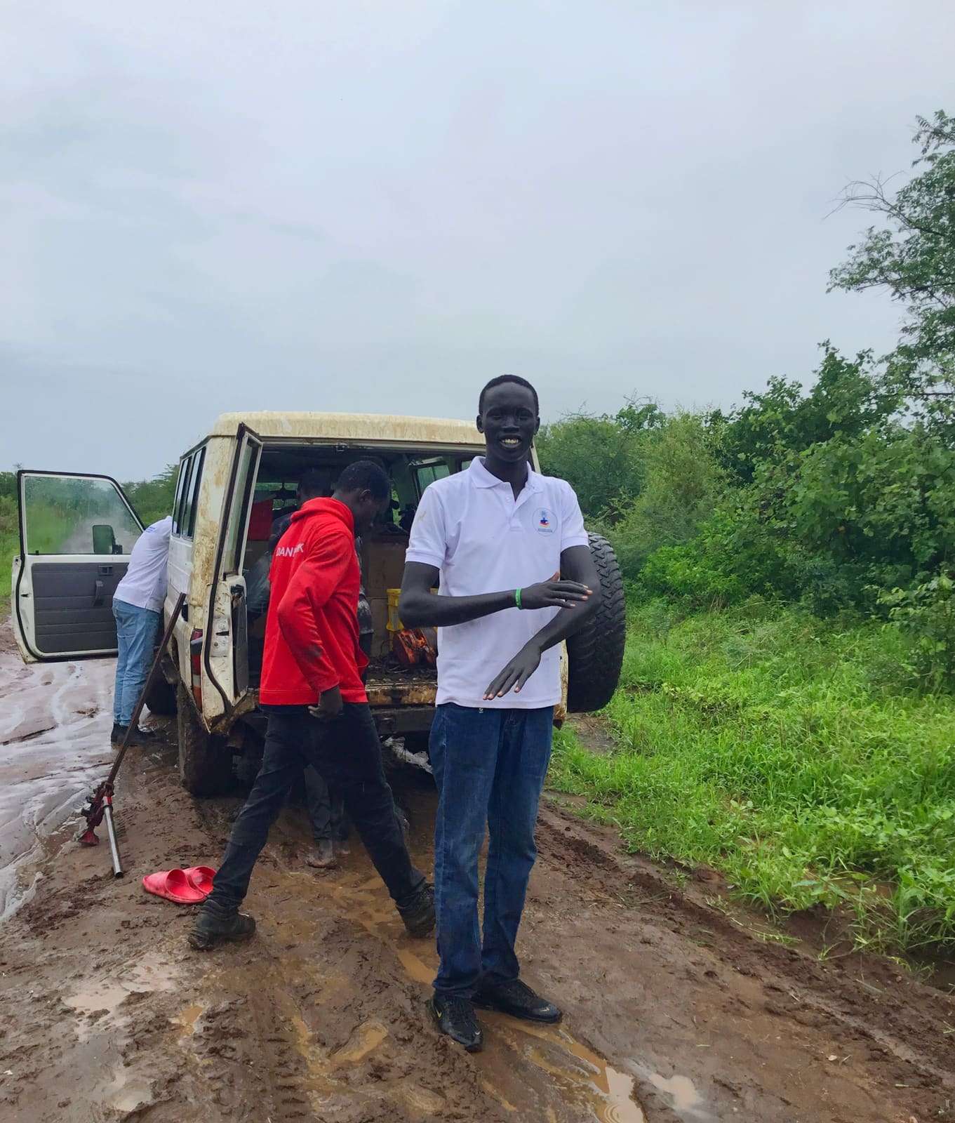 Team members on a field visit beside a vehicle on a muddy road